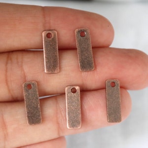 May include: Five antique copper-colored metal rectangular tags with a hole at the top. The tags have a distressed, aged look.