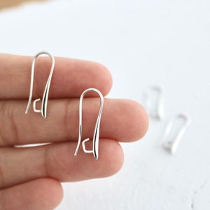 May include: Three silver earring hooks, also known as French hooks, are shown in a close-up image. The hooks are made of metal and have a smooth, polished finish.