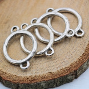 May include: Four silver-toned metal rings with three holes each. The rings are stacked on top of each other and have a hammered texture.