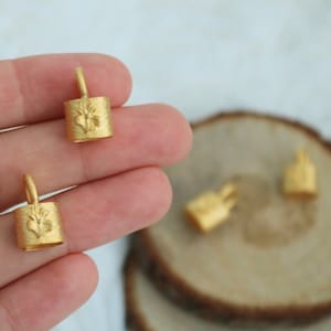 May include: Three gold-coloured metal charms with a floral design. The charms are in the shape of a small cylinder with a loop at the top.