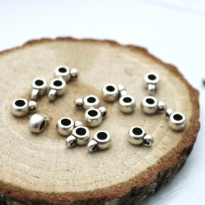May include: Silver metal bead caps with a loop on top. The bead caps are scattered on a wooden surface.