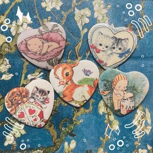 May include: Five heart-shaped ceramic ornaments with vintage illustrations. One features a baby sleeping in a flower, another a fawn, another two kittens, another a baby with a jar, and the last a pair of kittens.