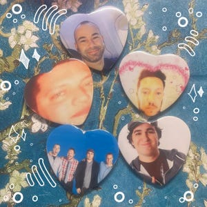 May include: A collection of five heart-shaped buttons, each featuring a different person's portrait. The buttons vary in color and design, with some showcasing individual faces and others a group of people. The background is a teal floral pattern.