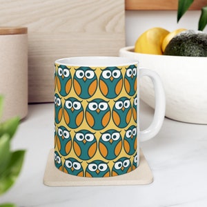 May include: A white ceramic mug with a yellow background and a repeating pattern of teal blue owls with orange beaks and white eyes.