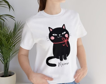 Puede incluir: Camiseta blanca con un gato negro con un lazo rojo y la palabra "Meow" impresa en la parte delantera.