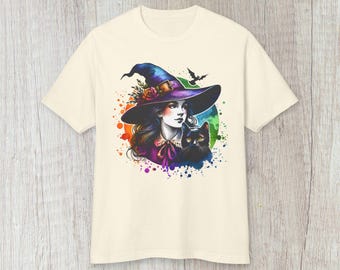 May include: A cream coloured t-shirt featuring a colourful graphic of a witch with a black cat. The witch is wearing a purple and black hat with flowers and a black dress. The graphic is surrounded by colourful paint splatters.