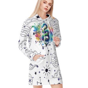 Puede incluir: Vestido con capucha blanco con un diseño de serpiente colorida dentro de un círculo, rodeado de estrellas, constelaciones y nubes. El vestido tiene mangas largas y un bolsillo delantero. El diseño incorpora un efecto acuarela con tonos vibrantes.
