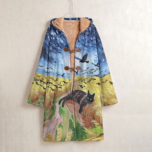 May include: A long-sleeved hooded coat featuring a printed landscape of a golden wheat field, a dark blue sky with birds, and a black cat. The coat has a tan faux-fur lining and two brown toggle closures on the front, hanging from a wire hanger.