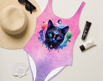 Op de afbeelding: Een roze en paarse ombre badpak met een zwarte kat illustratie. De kat heeft een derde oog en is omringd door een aquarel-achtig galaxy ontwerp.