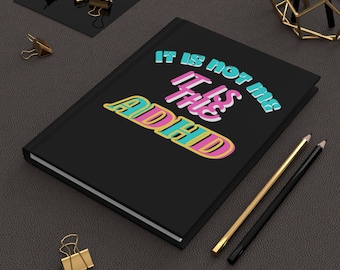 May include: Black notebook with the text "It is not me It is the ADHD" in colorful, stylized lettering.