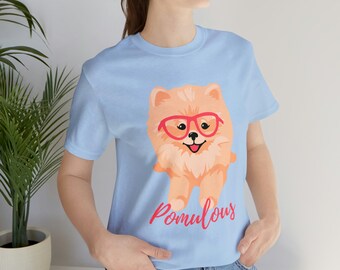 May include: A light blue t-shirt with a cartoon image of a Pomeranian dog wearing red glasses. The text "Pomulous" is printed in pink below the dog.
