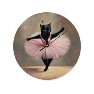 May include: Round wall clock featuring a black cat in a pink tutu, arms outstretched in a ballet pose. The clock face has black hands and a gold center, set against a neutral background. A whimsical decorative piece.