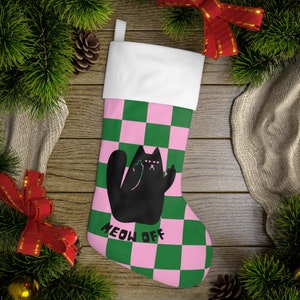 May include: Christmas stocking with a white cuff, featuring a pink and green checkerboard pattern. A black cat illustration with raised middle fingers is centered on the stocking, with the words "MEOW OFF" below.