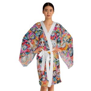 May include: A white robe with a colorful cat print. The robe has long sleeves and a tie belt. The cats are painted in a variety of colors and poses.
