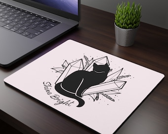 Puede incluir: Una alfombrilla de ratón blanca con un gato negro sentado encima de cristales. El texto "Shine Bright" está escrito debajo del gato.