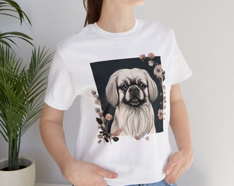May include: White t-shirt with a graphic of a small, light brown dog with black eyes and a black nose. The dog is surrounded by floral designs in shades of brown and pink.