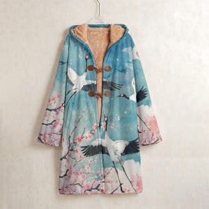 Puede incluir: Abrigo largo con capucha, con un diseño de grullas y flores de cerezo en tonos azules, blancos y rosas. El abrigo tiene un forro interior suave de color beige y se abrocha con tres cierres de palanca.