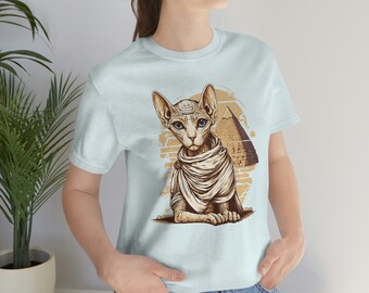 May include: A light blue t-shirt featuring a graphic of a sphinx cat wearing a white scarf in front of a pyramid. The cat has blue eyes and a brown nose.