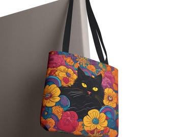 May include: A black cat with yellow eyes is nestled in a bed of colorful flowers. The tote bag is made of canvas and has black straps.