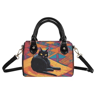 May include: A black handbag with a black cat illustration. The bag features a colorful geometric pattern on the front and a black handle. It has a detachable shoulder strap and gold-colored hardware.
