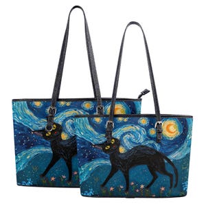 Puede incluir: Dos bolsos tote negros con una pintura de un gato negro sobre un fondo de cielo estrellado. Los bolsos tienen asas negras y hebillas plateadas. El gato tiene ojos amarillos y camina por un campo de flores.