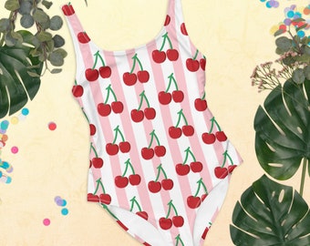 May include: One-piece swimsuit with a cherry pattern. The swimsuit features a white and pink striped background with red cherries and green stems. The straps are white and the swimsuit is sleeveless.
