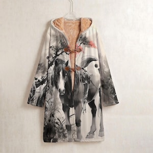 May include: A long, hooded coat with a horse illustration in shades of grey and white. The coat features a toggle closure and a soft, tan-coloured lining. The design includes a tree and floral elements.