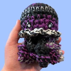 May include: A crocheted octopus plush toy with black, purple, and gray yarn. The octopus has large, black eyes with white pupils.