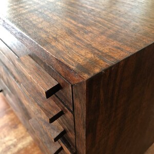 Puede incluir: Una caja de madera marr&oacute;n oscuro con varios cajones. Los cajones est&aacute;n apilados uno encima del otro y tienen un borde frontal ligeramente inclinado.