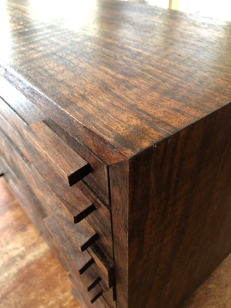 Puede incluir: Una caja de madera marr&oacute;n oscuro con varios cajones. Los cajones est&aacute;n apilados uno encima del otro y tienen un borde frontal ligeramente inclinado.