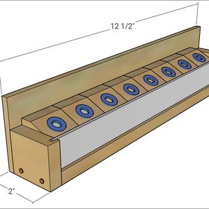 Puede incluir: Un soporte de herramientas de madera con un acabado marrón claro. Cuenta con una serie de inserciones circulares azules y blancas. El soporte mide 31,75 cm de largo, 5,08 cm de ancho y 6,99 cm de alto.