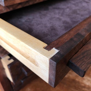 Puede incluir: Primer plano de un caj&oacute;n de madera con un interior de madera clara y un tirador de madera oscura. El caj&oacute;n est&aacute; abierto y el interior est&aacute; forrado con una tela marr&oacute;n oscura.