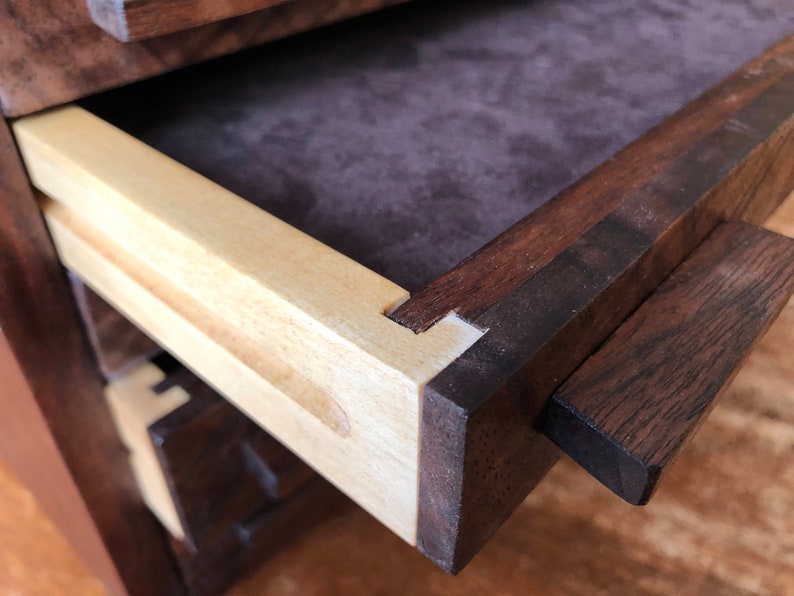 Puede incluir: Primer plano de un caj&oacute;n de madera con un interior de madera clara y un tirador de madera oscura. El caj&oacute;n est&aacute; abierto y el interior est&aacute; forrado con una tela marr&oacute;n oscura.