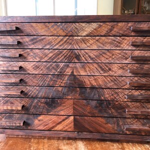 Puede incluir: Un armario de cajones de madera con ocho cajones y veta de madera marr&oacute;n oscuro. Los cajones tienen tiradores rectangulares simples.