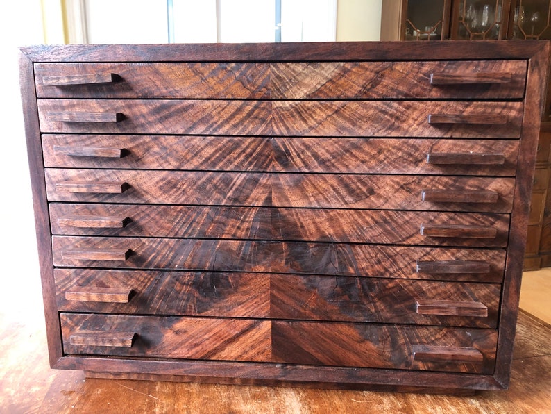 Puede incluir: Un armario de cajones de madera con ocho cajones y veta de madera marr&oacute;n oscuro. Los cajones tienen tiradores rectangulares simples.