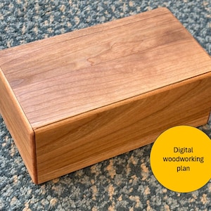 Könnte beinhalten: Eine rechteckige Holzkiste mit hellbraunem Finish. Die Kiste hat eine glatte, polierte Oberfläche und ist aus hellem Holz gefertigt. Ein gelber Kreis mit dem Text "Digital woodworking plan" befindet sich in der unteren rechten Ecke.