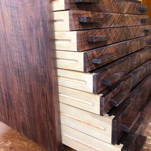 Puede incluir: Una caja de madera con varios cajones que se abren para revelar un interior de madera clara. La caja est&aacute; hecha de madera oscura con un acabado marr&oacute;n oscuro.