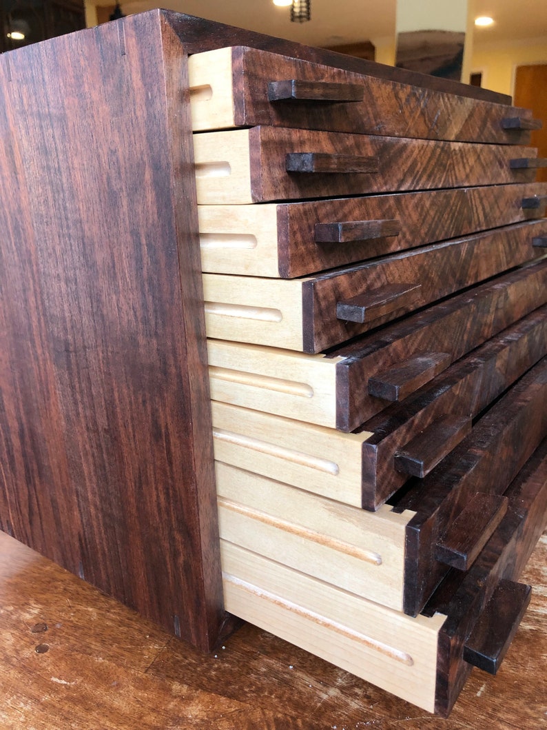 Puede incluir: Una caja de madera con varios cajones que se abren para revelar un interior de madera clara. La caja est&aacute; hecha de madera oscura con un acabado marr&oacute;n oscuro.