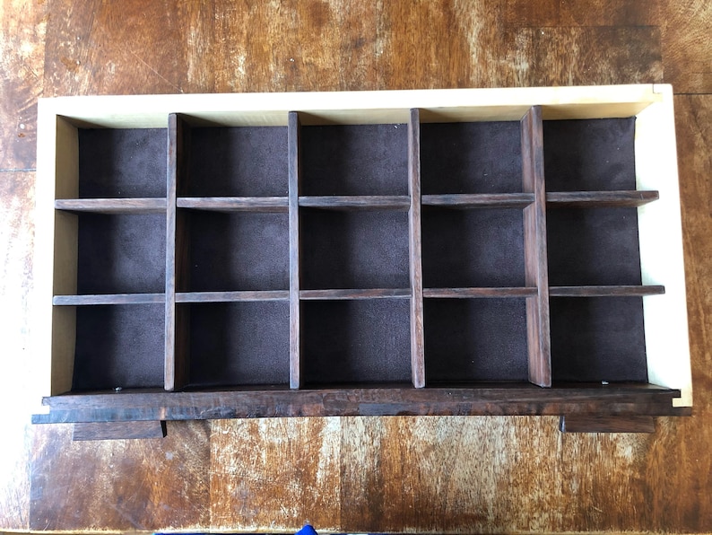 Puede incluir: Una caja de madera con un forro de fieltro marr&oacute;n y 16 compartimentos individuales. La caja est&aacute; hecha de madera clara y oscura.