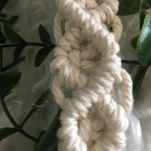 May include: A close-up of a white macrame wall hanging with a repeating pattern of circles. The macrame is made with thick cotton cord.