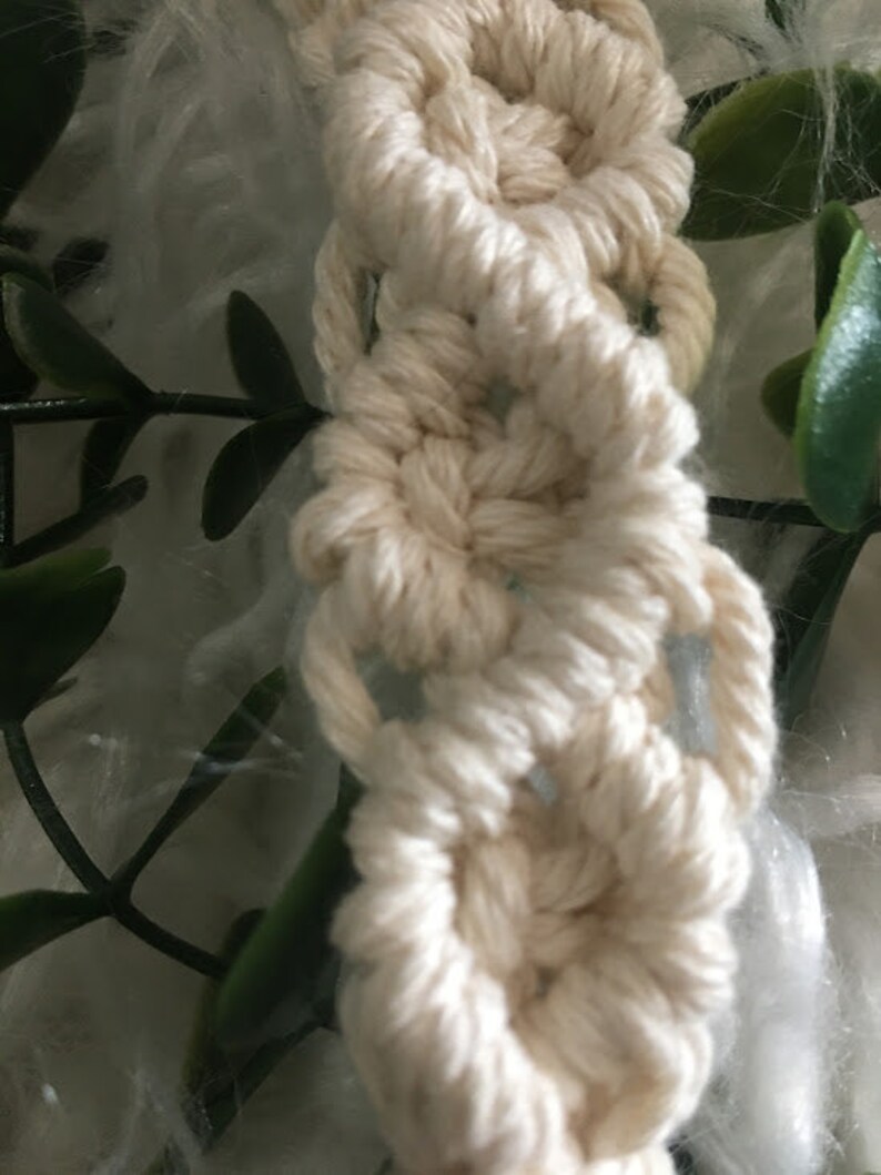May include: A close-up of a white macrame wall hanging with a repeating pattern of circles. The macrame is made with thick cotton cord.