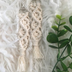 May include: Two white macrame keychains with silver key rings and tassels. The keychains are made with a knotting technique and have a geometric pattern.
