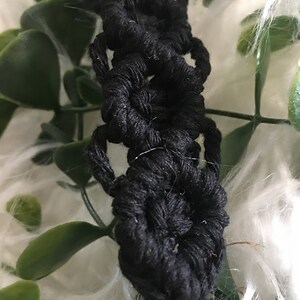 May include: Black macrame keychain with a silver ring. The keychain is made of a thick, knotted cord and features a series of circular designs.