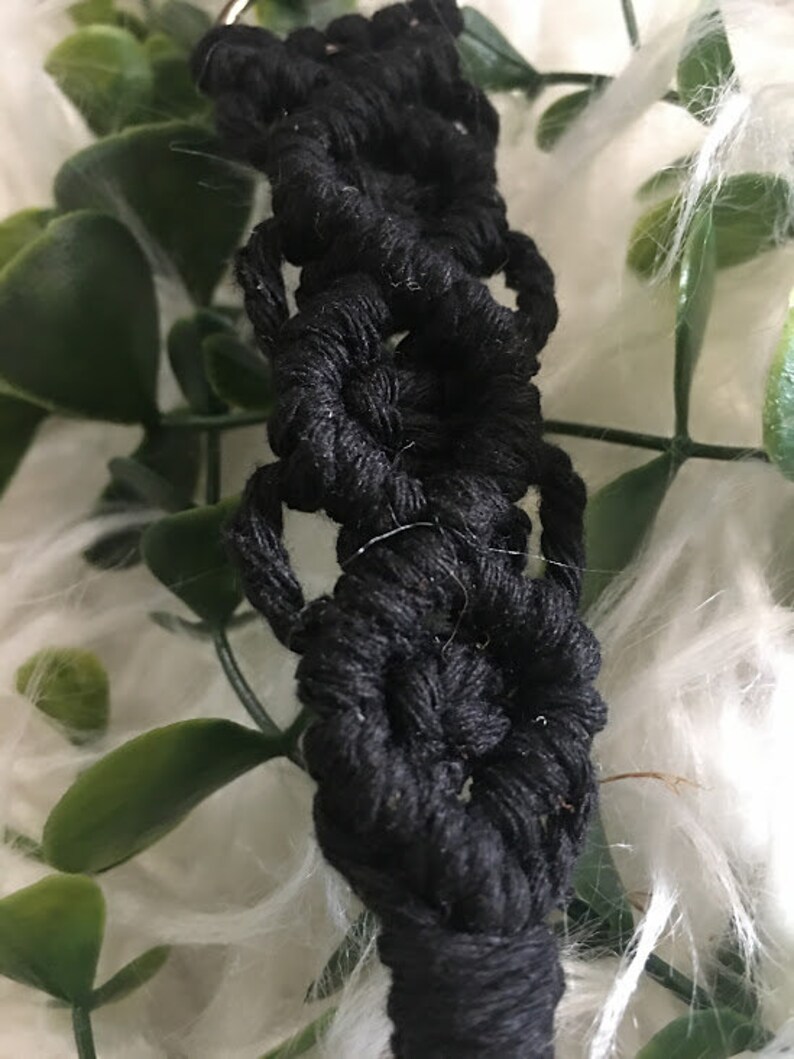 May include: Black macrame keychain with a silver ring. The keychain is made of a thick, knotted cord and features a series of circular designs.