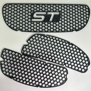 May include: Three black plastic car grille inserts with a honeycomb pattern. The top insert has the letters "ST" in white.