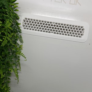 May include: A white rectangular vent with a honeycomb pattern is set into a white surface. The text "VIV-TEK-UK" is above the vent. Green leafy vines are in the left corner.