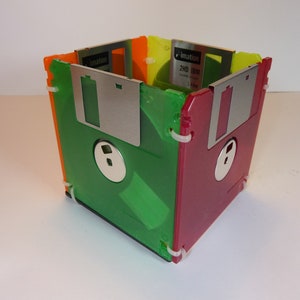 May include: A colourful desk organiser made from six 3.5-inch floppy disks. The disks are green, red, orange, and yellow. The organiser is assembled with white plastic ties.