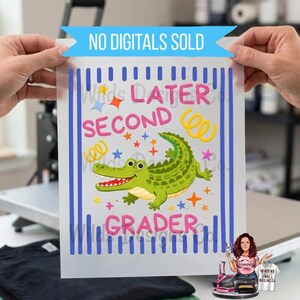Pu&ograve; includere: Un foglio di vinile termotrasferibile con la scritta "Later Second Grader" e un alligatore dei cartoni animati. Il disegno comprende stelle, coriandoli e strisce verticali blu. Lo striscione in alto recita "NO DIGITALS SOLD".