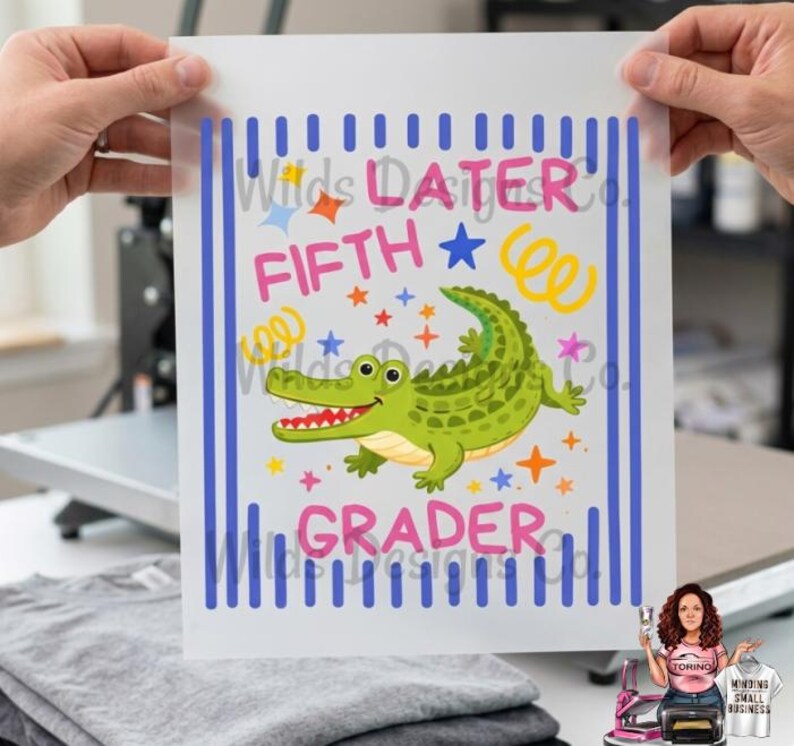 Pu&ograve; includere: Un foglio di trasferimento termico con un alligatore verde dei cartoni animati e le parole "LATER FIFTH GRADER" in rosa e blu. Il design include stelle e spirali, con strisce verticali blu sui lati.