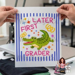 Pu&ograve; includere: Un foglio di trasferimento bianco con un design colorato con un alligatore verde, stelle e le parole "Later First Grader". Il design &egrave; incorniciato da strisce verticali blu.